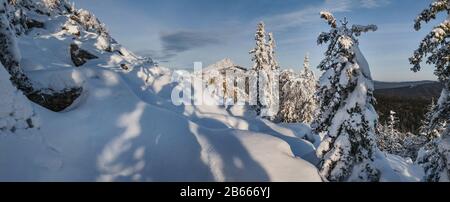 Idillische Berglandschaft mit Schneeverwehungen und schneebedeckten Bäumen Stockfoto