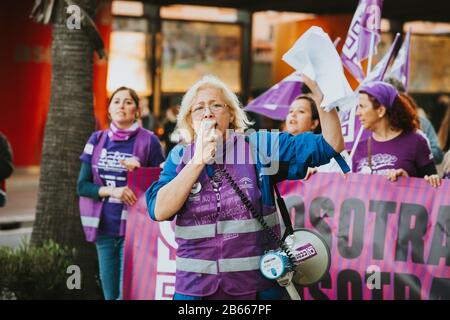 Málaga, SPANIEN - 8. MÄRZ 2020: Alte Frau, die während des feministischen Streiks in Málaga, Spanien, am 8. März 2020 mit einem Megafon in der Hand schreit. Stockfoto