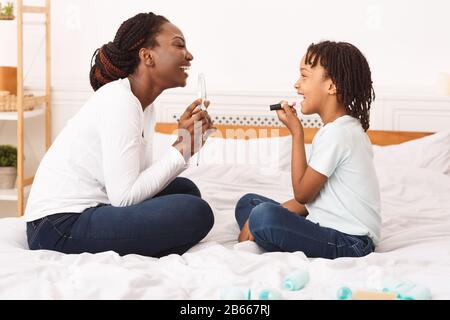 Kleines afro-Mädchen, das mit ihrer Mutter im Schlafzimmer Make-up macht Stockfoto