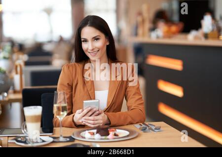 Geschäftsfrau mit Smartphone beim Mittagessen im Café Stockfoto