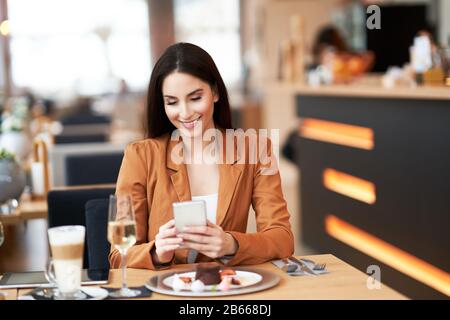 Geschäftsfrau mit Smartphone beim Mittagessen im Café Stockfoto