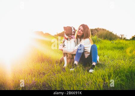 Attraktive lächelnde Frau umarmt ihren schönen Hund. American Stranford Stockfoto