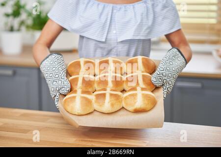 Fröhliche Erwachsene Frau bereitet in der Küche heiße Kreuzbrötchen für Ostern vor Stockfoto