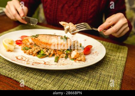 Mädchen mit Gabel und Messer in den Händen, die Lachssteak mit Reis und Gemüse im Restaurant essen Stockfoto