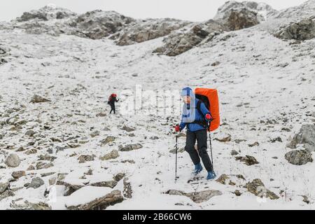 Kletterer, der auf einem steilen, schneebedeckten Hang in den Bergen auf dem Hintergrund einer Klippe und des Abgrunds spazieren geht. Das Konzept von Risiko und Abenteuer im Freien Stockfoto