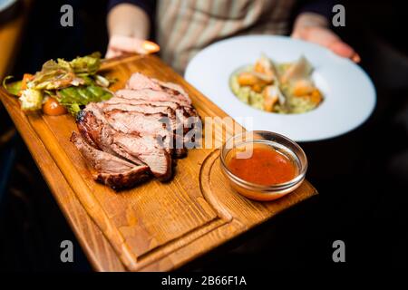 Frisch zubereitetes Fleischsteak in Stücke auf einem Holzbrett geschnitten. Serviert mit Sauce und grünem Salat. Stockfoto