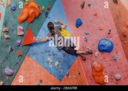 Professioneller Kletterer, der im Innenbereich an einer künstlichen Wand mit Felsbrocken trainiert Stockfoto