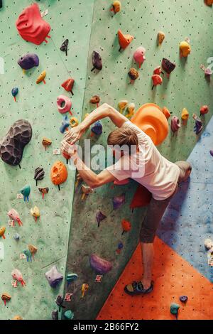 Professioneller Kletterer, der im Innenbereich an einer künstlichen Wand mit Felsbrocken trainiert Stockfoto