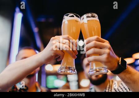 Freunde, die im Pub mit einer Brille helles Bier toben. Eine Gruppe junger Leute, die sich an der Bar entspannen. Stockfoto