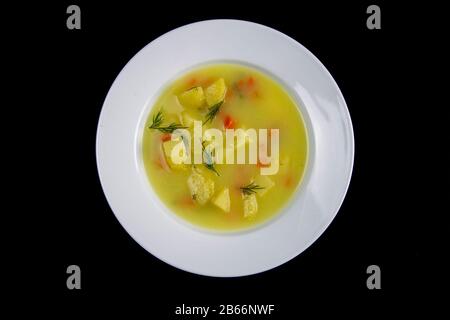 Weiße Milchsuppe mit Kartoffeln, Karotten, Grüns steht in einer weißen Platte, die auf schwarzem Grund isoliert ist Stockfoto