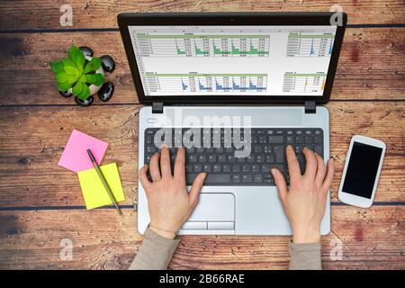Draufsicht über Frauen, die zu Hause auf einem Laptop arbeiten und Zahlen in eine Tabelle eingeben Stockfoto