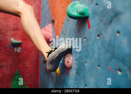 Fuß in Kletterschuhen eines Mannes auf künstlichem Felsbrocken im Fitnessstudio Stockfoto