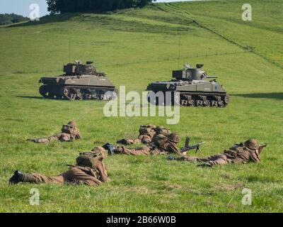 Aktuelle Soldaten des Royal Anglian Regiment im WW2-Kit, die eine Infanterieplatonen-Attacke mit Unterstützung von Sherman-Panzern durchführen. Stockfoto