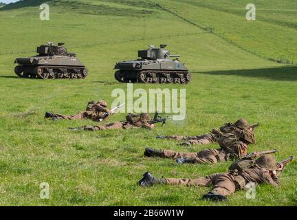 Aktuelle Soldaten des Royal Anglian Regiment im WW2-Kit, die eine Infanterieplatonen-Attacke mit Unterstützung von Sherman-Panzern durchführen. Stockfoto