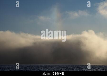 Blick auf den kleinen Regenbogen, der Sonnenhundeeffekt über den Morgennebel genannt wird, der über den Fjord steigt. Stockfoto
