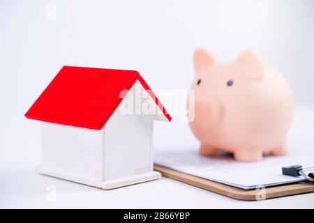 Finanzklage - Piggy Bank, wunderschönes rot-weißes Holzhausmodell auf weißem Hintergrund, spart Geld beim Kauf von Versicherungen, Nahaufnahme, Kopierplatz. Stockfoto