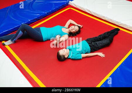 Schöne junge Mutter und kleiner Sohn, die auf dem Spielplatz spielen und auf einem Trampolin liegen Stockfoto