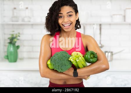 Glückliches junges afrikanisches Mädchen, das grüne Vegetale hält Stockfoto