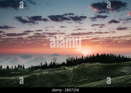 Schöner Sonnenuntergang in den Bergen mit Nebel und Wolken und kleinen Häusern Hirten Stockfoto