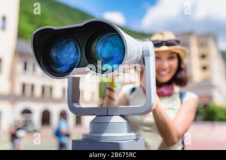 Frau Touristin bewundert die Aussicht auf die Resortarchitektur der Stadt durch ein Fernrohr auf der Straße Stockfoto