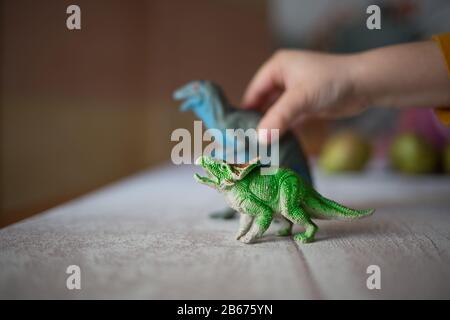 Kind zu Hause, das mit zwei Dinosauriern spielt. Differentieller Fokus weißer Hintergrund. Kindheitskonzept. Verschwommene Details Stockfoto