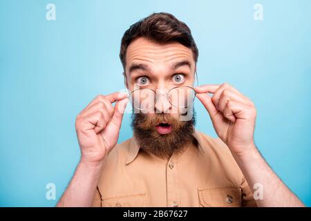 Nahaufnahme der staunenden Jugend, die ihre Spezeln berührt und ein braunes Hemd trägt, das über blauem Hintergrund isoliert ist Stockfoto