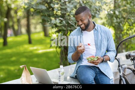 Black Guy, Der Draußen Mitnahme-Salat Isst Und Videos Auf Dem Laptop Ansieht Stockfoto