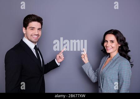 Porträt eines schönen Mannes und einer Frau mit welligem, geschweiften brunet-haar, das auf den Kopierbereich zeigt und eine schwarze Blazer Tuxedo-Jacke trägt, die über Grau isoliert ist Stockfoto