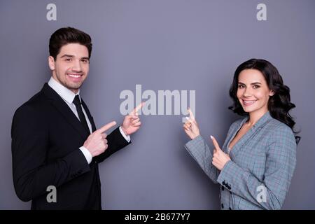 Porträt von charmanten Geschäftsleuten mit gewellter, lockiger Brunette-Frisur, die auf den Kopierbereich zeigt, mit schwarzem, stilvollem Blazer in der Jacke, isoliert über Stockfoto