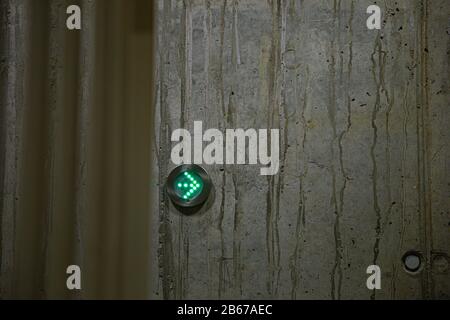 Grüner Pfeil als Richtzeichen in LED leuchtet in einem Metallring an einer Betonwand Stockfoto