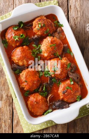 Hausgemachte Fleischbällchen mit Wildpilzen und Tomatensauce in einer Backform auf dem Tisch. Vertikale Draufsicht von oben Stockfoto