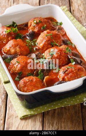 Gebackene Fleischbällchen mit Wildpilzen in Tomatensauce in einer Pfanne auf dem Tisch. Vertikal Stockfoto
