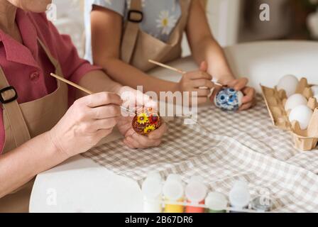 Granny mit ihrem Enkelkind, das Ostereier zusammen in der Küche malt, in der Nähe Stockfoto