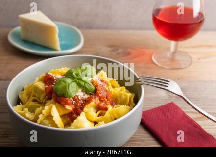 Hausgemachtes Dinner Tortellini mit Tomatensauce arrabbiata und Käse mit einem Glas Wein auf der Seite. Stockfoto