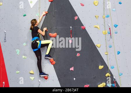 Schöne junge Frau beginnt, große künstliche Wand zu erklimmen Stockfoto