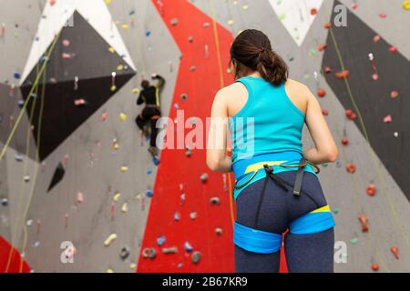 Sportfrau an der Kletterwand im Fitnessstudio, die ihren Freund auf der Strecke betrachtet Stockfoto