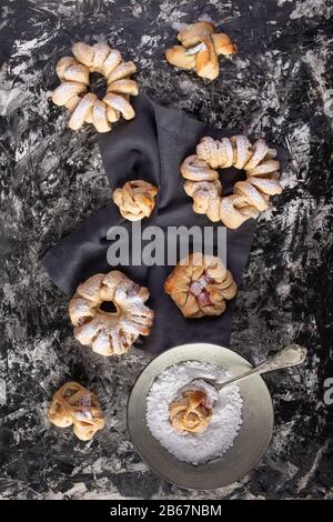 Brioches mit Puderzucker auf dunklem Hintergrund flach gelegt Stockfoto