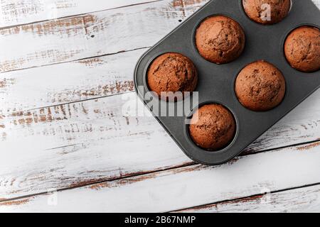 Frische Muffins in einer Backform auf einer Holzoberfläche, von oben beschossen. Stockfoto