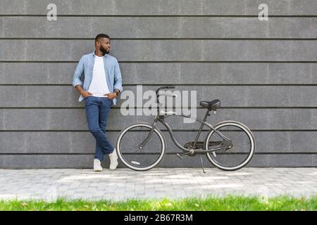 Afro Man Mit Stylischem Fahrrad, Das Über Der Grauen Urbanen Wand Posiert Stockfoto