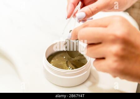 Weibliche Hände nehmen mit der Pinzette Augenflecken aus dem Behälter. Anti-Aging-Konzept. Stockfoto