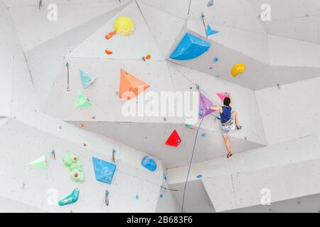 Sportler oder Amateur beginnen mit dem Klettern an einer großen Kunstwand in der modernen bunten Indoor-Boulder-Sporthalle Stockfoto