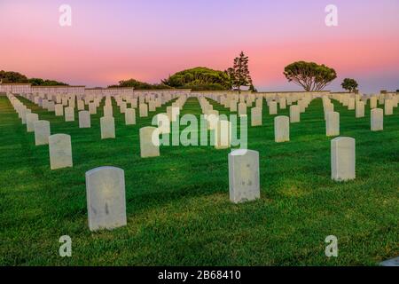 San Diego, Kalifornien, Vereinigte Staaten - 31. Juli 2018: Friedhof Friedhofsgräveyard weiße Grabsteine mit Sonnenstrahlen in orangefarbenem Himmel bei Sonnenuntergang. Amerikanischer Kriegsfriedhof in Stockfoto