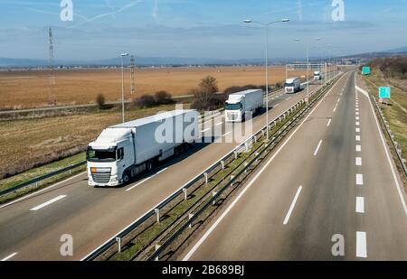 Konvoi weißer Transportwagen in Reihe als Karawane oder Konvoi auf einer Landstraße auf dem Land unter blauem Himmel Stockfoto