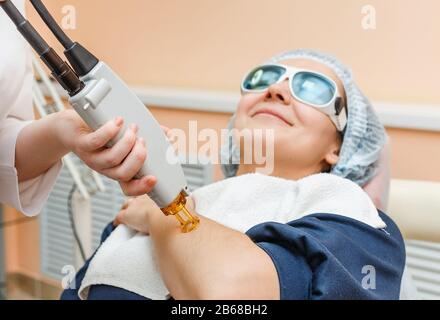 Der Kosmetologe des Arztes führt das Verfahren mit einem professionellen Lasersystem für Erwachsene Frauen durch. Laserepilation und -Behandlung Stockfoto