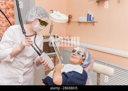 Der Kosmetologe des Arztes führt das Verfahren mit einem professionellen Lasersystem für Erwachsene Frauen durch. Laserepilation und -Behandlung Stockfoto