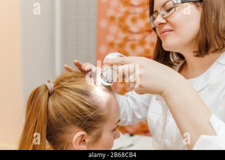 Doktor untersucht die Kopfhaut eines jungen Mädchens mit einem speziellen Dermatologiesystem, einem Haarausfall- und Trichologiekonzept Stockfoto