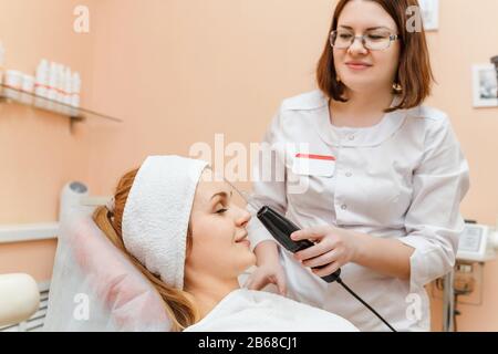 Schöne Frau, die eine moderne Darsonvaltherapie in der Klinik für Kosmetologie bekommt Stockfoto