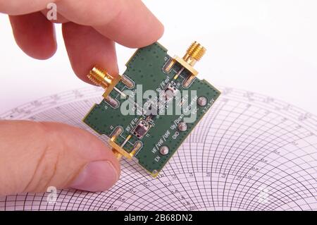 Hochfrequenztechniker prüfen die Leiterplatte der Mikrowellenmischer-Platine vor der Smith-Karte Stockfoto