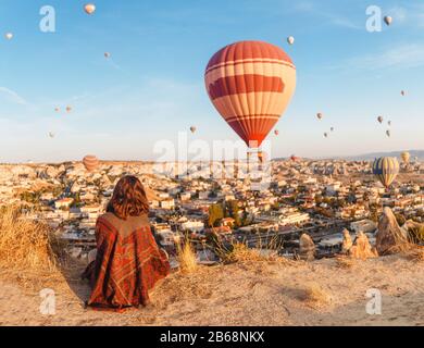 Ein Touristenmädchen auf einem Berggipfel mit wunderbarem Blick auf den Sonnenaufgang und die Luftballons in Kappadokien. Happy Travel in der Türkei Konzept Stockfoto
