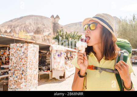 Junge Touristin mit Rucksack und Hut, die Eiscreme in der menschenleeren Landschaft des mittleren Ostens genießt Stockfoto